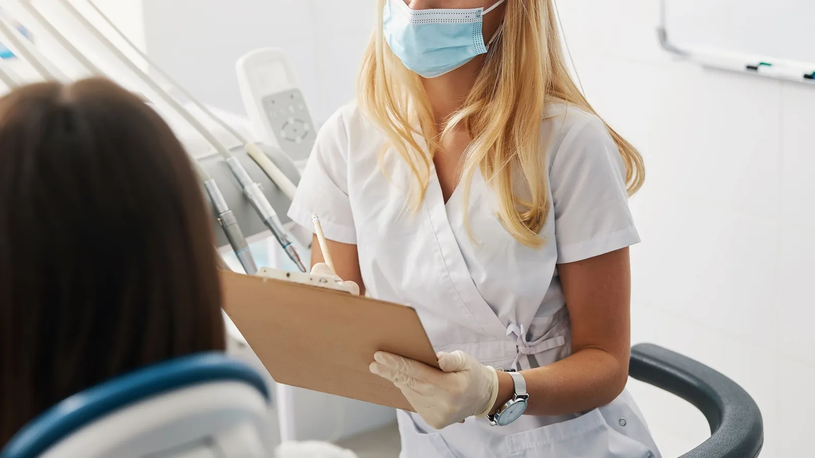 A clinician with a clipboard talking with a patient in the dental chair